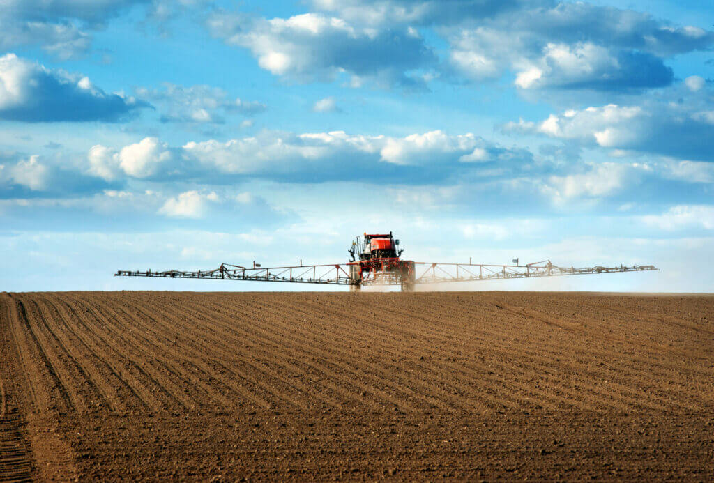Big red sprayer with long arms at the arable field makes fertilizers in early spring view with cloudy sky